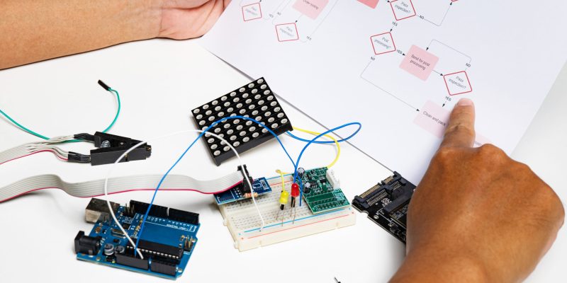 back view hands open flowchart sitting at desk using onboard programming debug improve binary algorithm code in workstation focusing on devices and blurring people